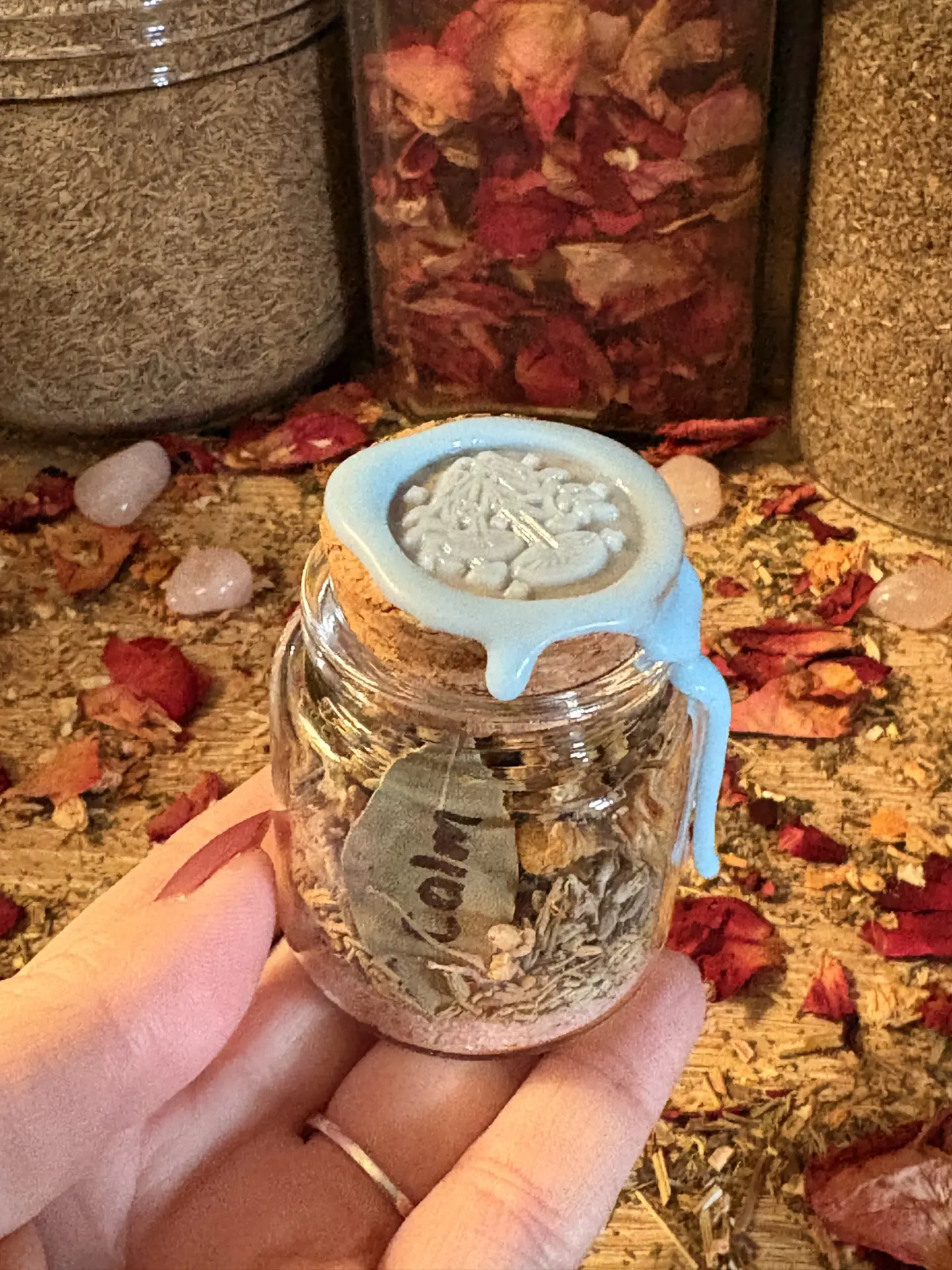 Hand holding a small glass spell jar sealed with blue wax